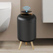 Black cylindrical device with gold legs on a wooden floor against a beige wall.