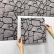 Hands holding a stone-patterned wall panel against a matching wall.