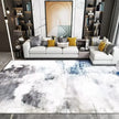 Modern living room with a gray sofa, colorful pillows, and an abstract patterned rug.