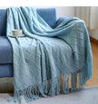 Light blue textured throw blanket draped over a sofa with a cup on a small table.