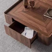 Wooden side table with an open drawer containing a magazine on a gray carpet.