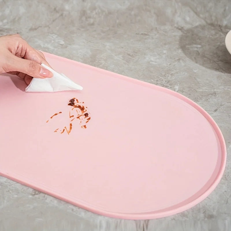 Pink mat with a hand using a white cloth to wipe up a spill on a gray surface.