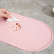 Pink mat with a hand using a white cloth to wipe up a spill on a gray surface.