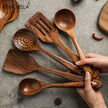 Set of wooden kitchen utensils with a hand holding them on a gray surface, featuring the KEMORELA brand.