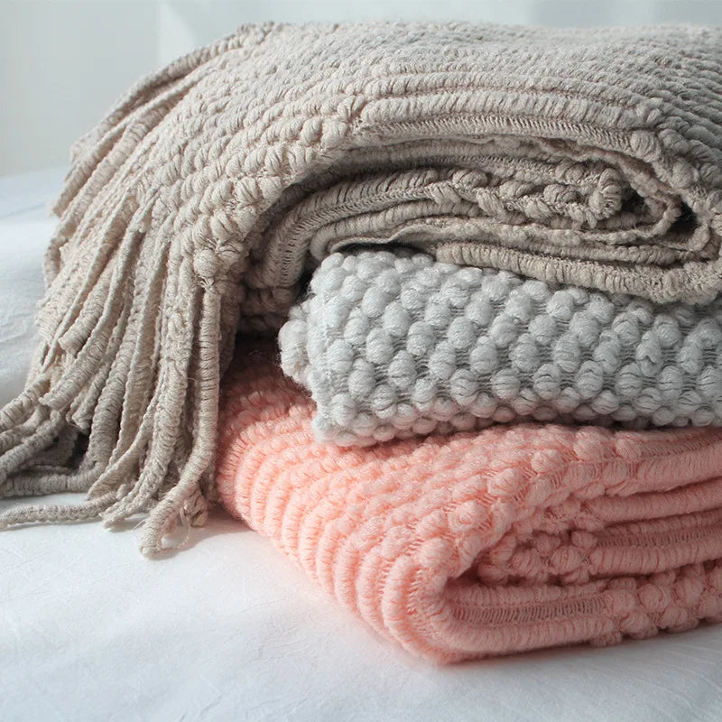 Stack of textured blankets in beige, gray, and pink on a light background