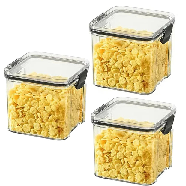 Three square storage containers with lids filled with yellow cereal on a white background
