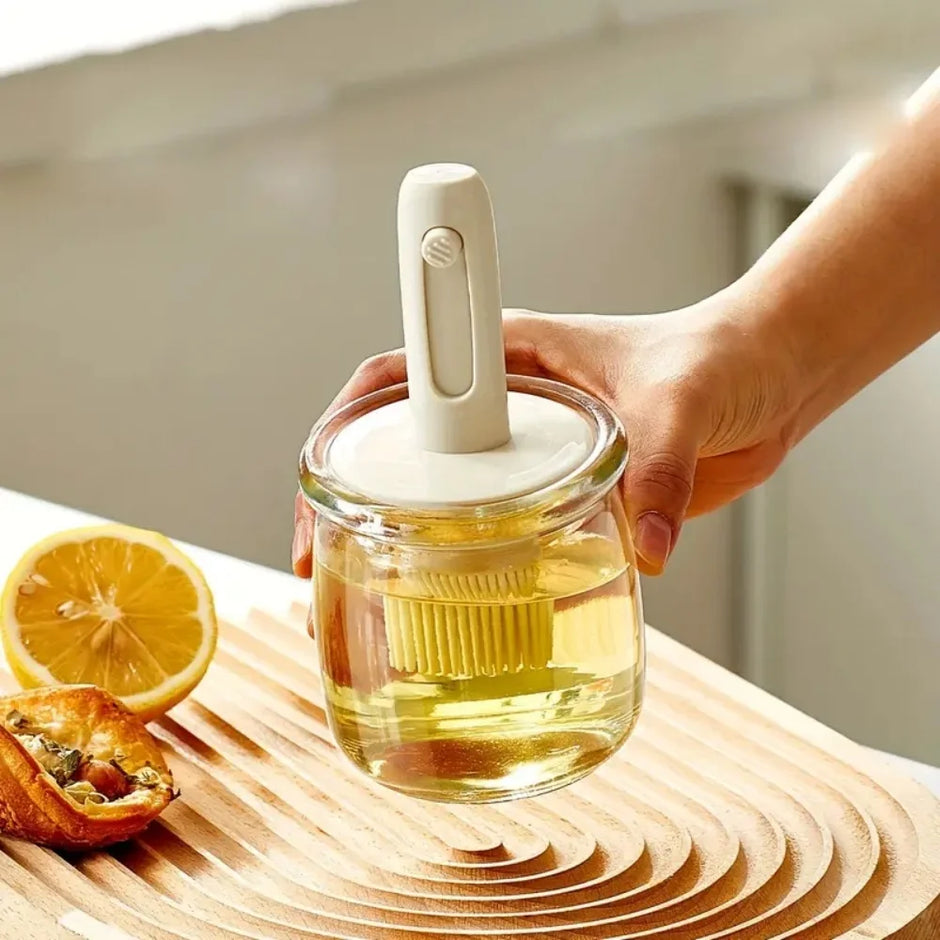 Hand holding a glass jar with a white lid and handle, containing a yellow liquid, on a wooden surface with a lemon and bread.