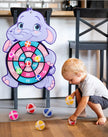 Child playing with a dartboard shaped like an elephant in a home setting