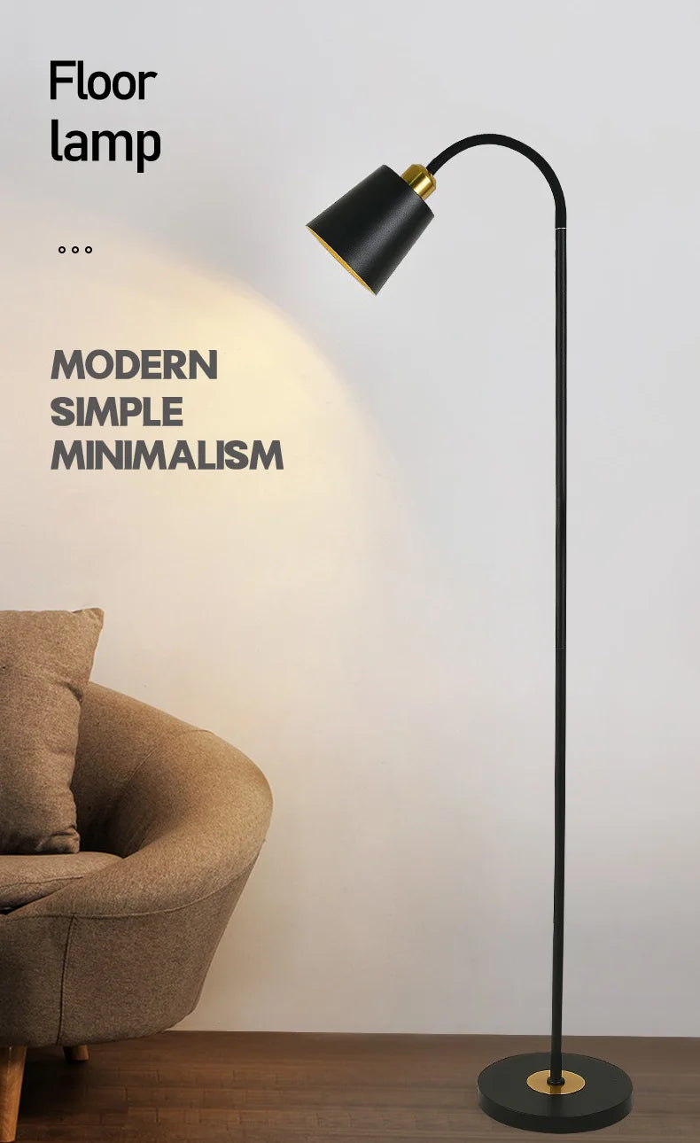 Modern floor lamp with black and gold design next to a brown armchair on a light gray background.