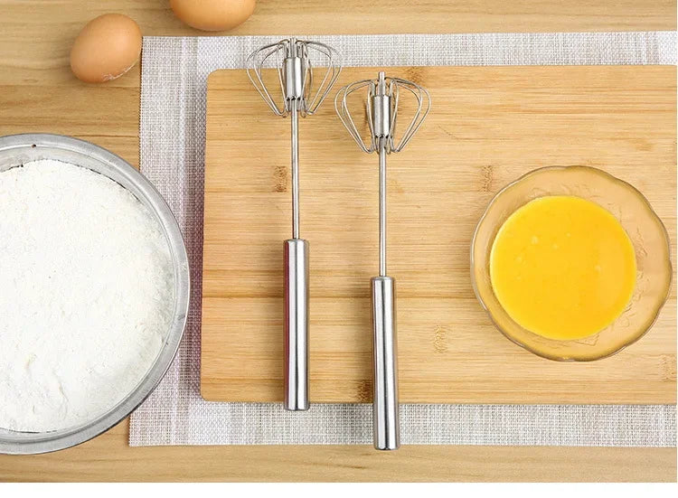 Two metal beaters on a wooden cutting board with eggs, flour, and a bowl of yellow mixture.