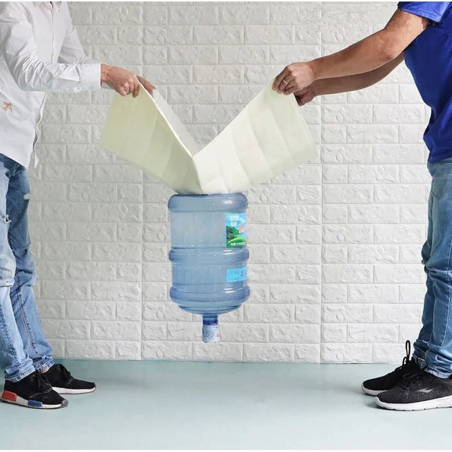 Two people pouring water from a large blue container into a smaller green container against a white brick wall.