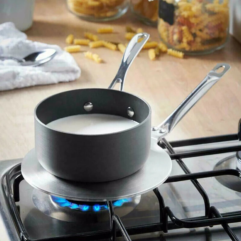 Black saucepan on a gas stove with milk inside, surrounded by jars and a towel on a wooden surface.