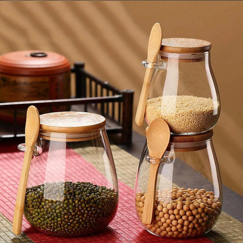 Two glass jars with wooden lids and spoons on a red mat, containing different types of beans.