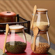 Two glass jars with wooden lids and spoons on a red mat, containing different types of beans.