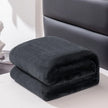 Folded dark gray blanket on a white surface with a blurred background