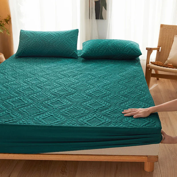 Teal quilted mattress cover on a bed with pillows in a room setting.