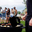 Person grilling outdoors with friends in the background