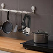 Kitchen utensils and pots hanging on a rack against a tiled wall.