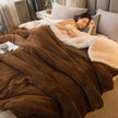 Woman lying on a bed under a brown and white comforter with a side table in the background.