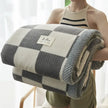 Person holding a checkered blanket with a visible brand label against a white curtain background