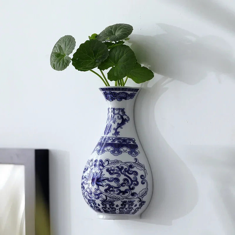 Blue and white decorative vase with green plant on a white surface
