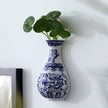 Blue and white decorative vase with green plant on a white surface