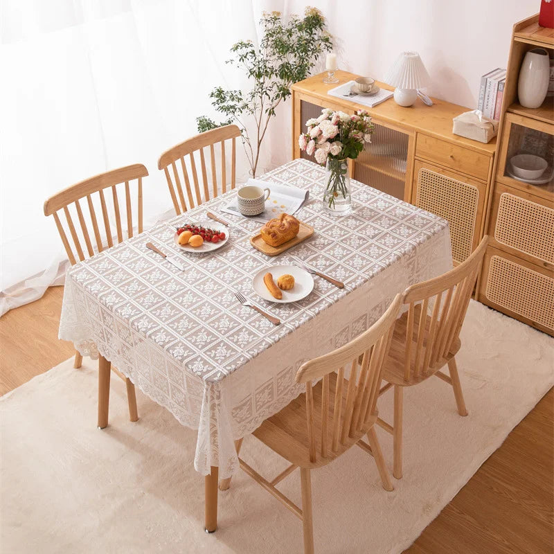 Dining table set with a lace tablecloth, chairs, and food in a bright room.