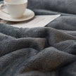 Gray textured blanket with a cup of tea and saucer in the background