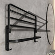 Black towel rack mounted on a gray tiled wall with a round mirror to the right.
