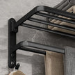 Black towel rack mounted on a gray tiled wall with towels hanging from it.