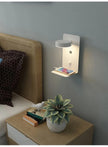 Wall-mounted night light with a shelf above a bedside table in a bedroom setting.