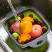 Collapsible fruit and vegetable sink basket with fruits being washed under running water.