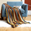 Colorful zigzag patterned blanket draped over a blue armchair with books on a white surface.