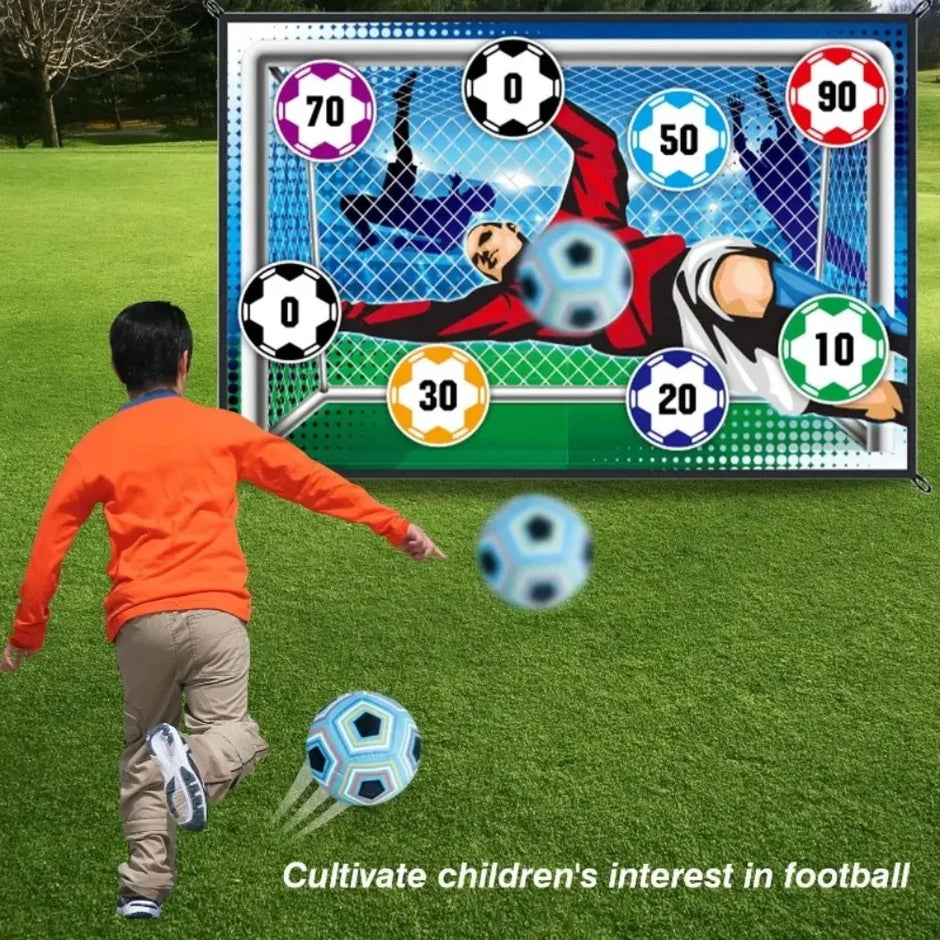 Person playing with a soccer ball in front of an electronic goal scoring display on a grassy field.