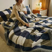 Person sitting on a bed with a patterned blanket, holding a cup.