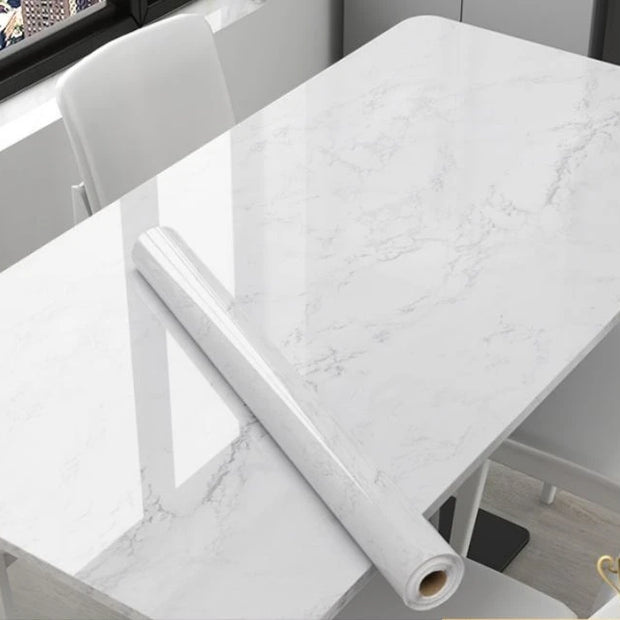 Roll of marble-patterned vinyl wrap on a table with chairs in the background