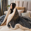 Woman wrapped in a large gray blanket with beige lining on a bed.