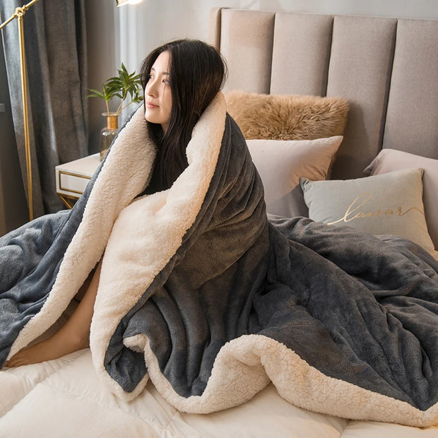 Woman wrapped in a large gray blanket with beige lining on a bed.