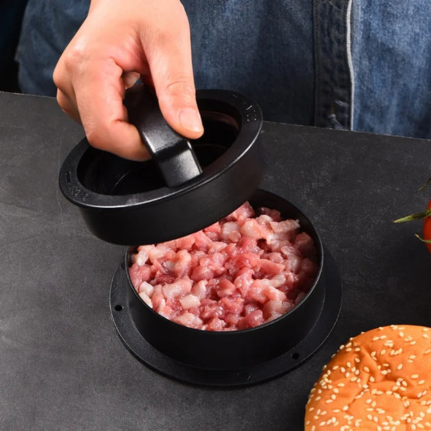 Hand using a black meat grinder to make ground meat on a dark surface with a hamburger bun in the foreground.