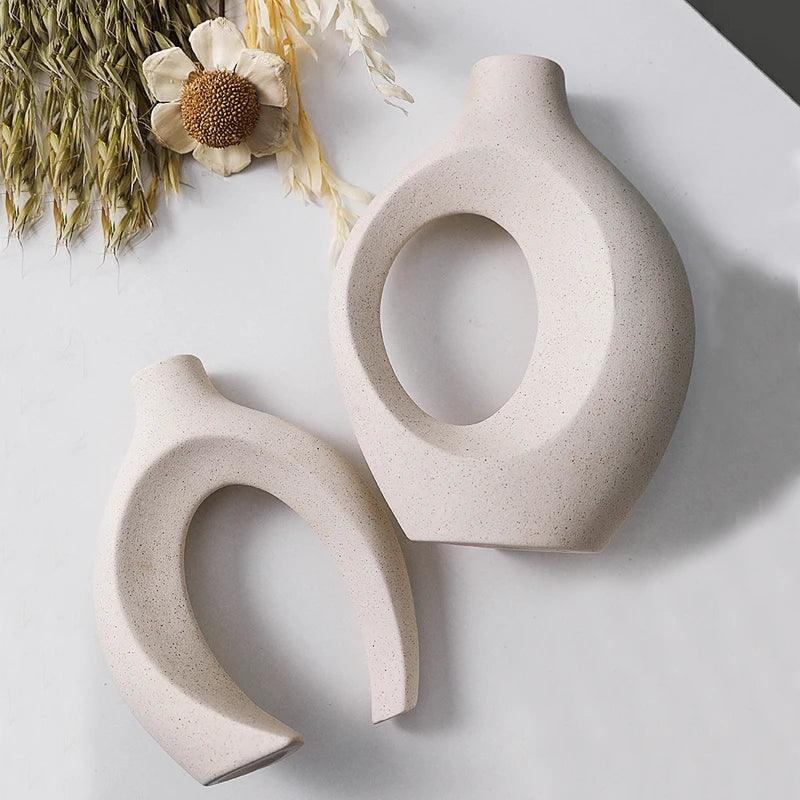 Two beige ceramic vases on a light surface with dried flowers.