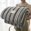 Person holding a striped blanket with a visible brand label against a light background