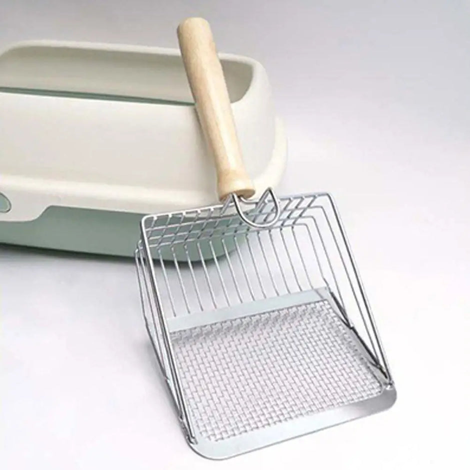 Metal scoop with wooden handle next to a cat litter box on a light gray background