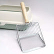 Metal scoop with wooden handle next to a cat litter box on a light gray background
