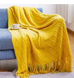 Yellow blanket draped over a blue sofa with a cup on a small table.
