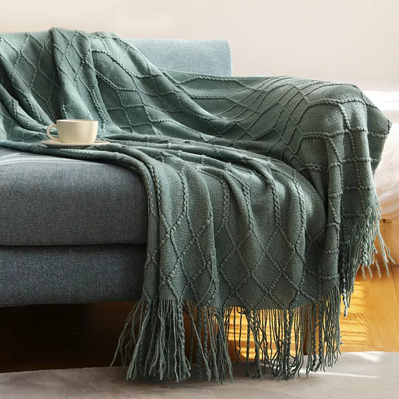 Green textured throw blanket draped over a gray sofa with a cup on a small table.