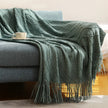 Green textured throw blanket draped over a gray sofa with a cup on a small table.