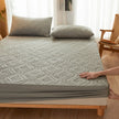 Person adjusting a textured mattress cover on a bed with pillows in a room.