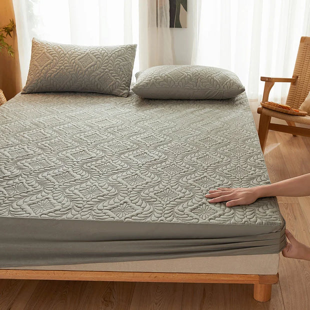 Person adjusting a textured mattress cover on a bed with pillows in a room.