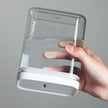 Hand holding a clear plastic container with a white base against a gray background