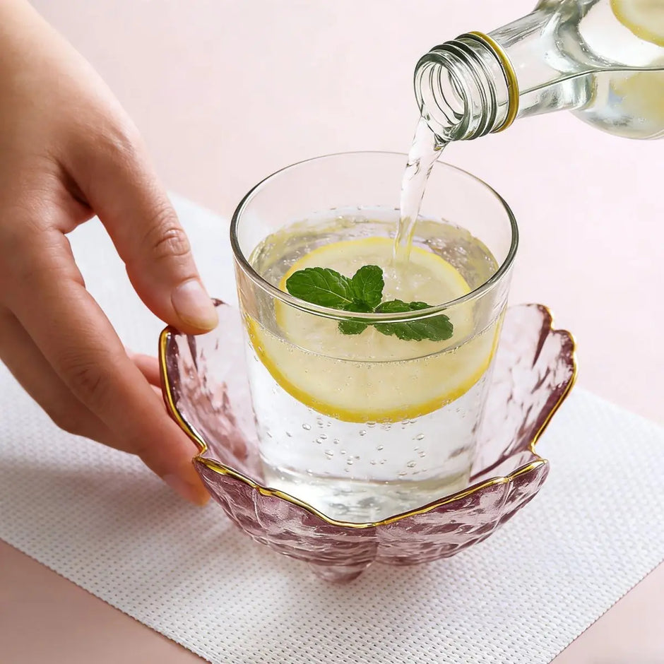Hand pouring liquid into a glass with lemon and mint on a light pink background